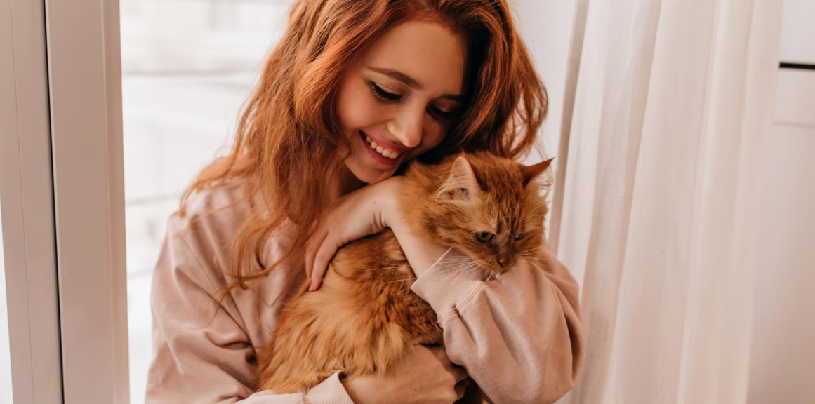 Imagem de uma mulher ruiva abraçada em seu gato de pelos avermelhados