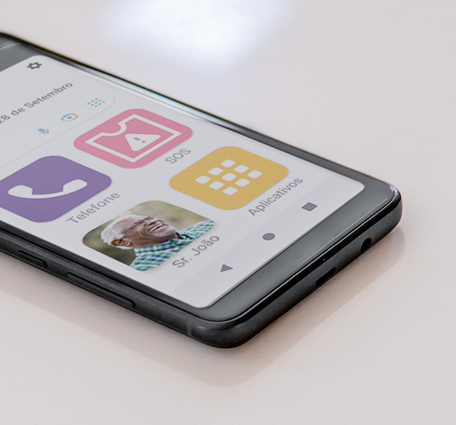 A imagem mostra a tela de um smartphone com ícones grandes e simplificados, indicando ser uma interface adaptada para idosos. Os ícones estão em português, com "Telefone", "SOS" e "Aplicativos", e há um contato chamado "Sr. João" com a foto de um senhor sorridente.