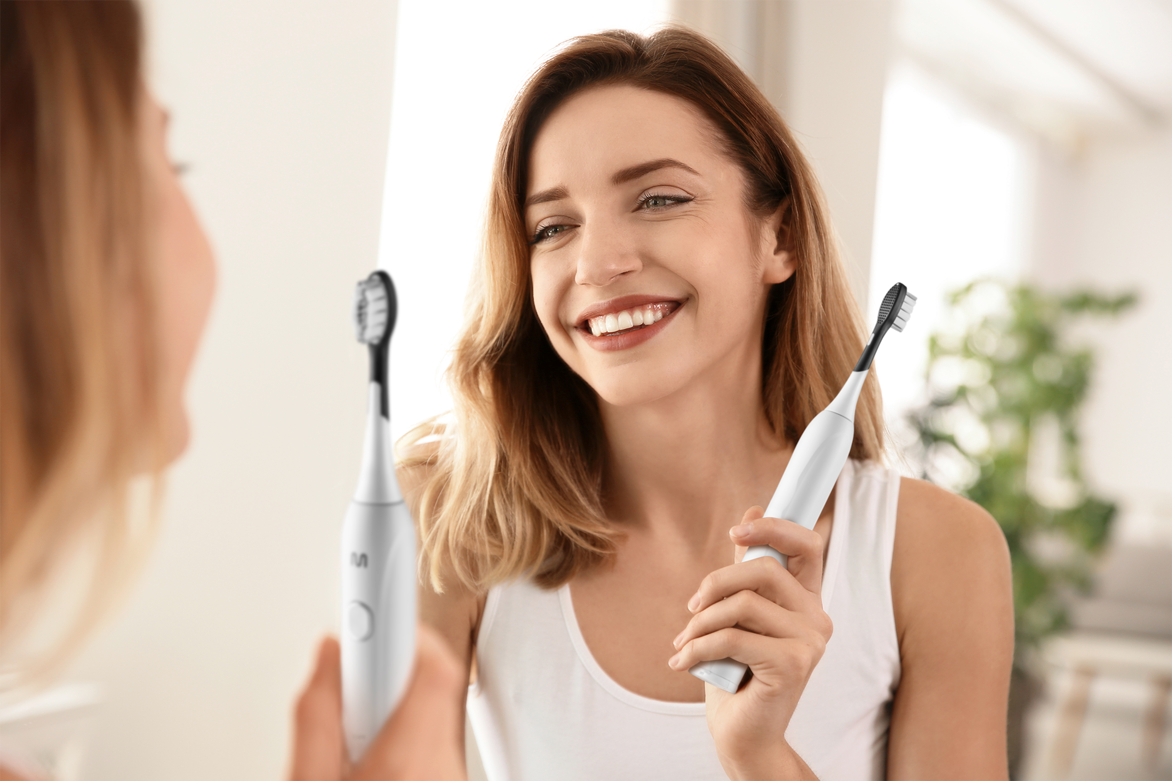 Mulher sorrindo em frente a um espelho com a escova dental elétrica Multi