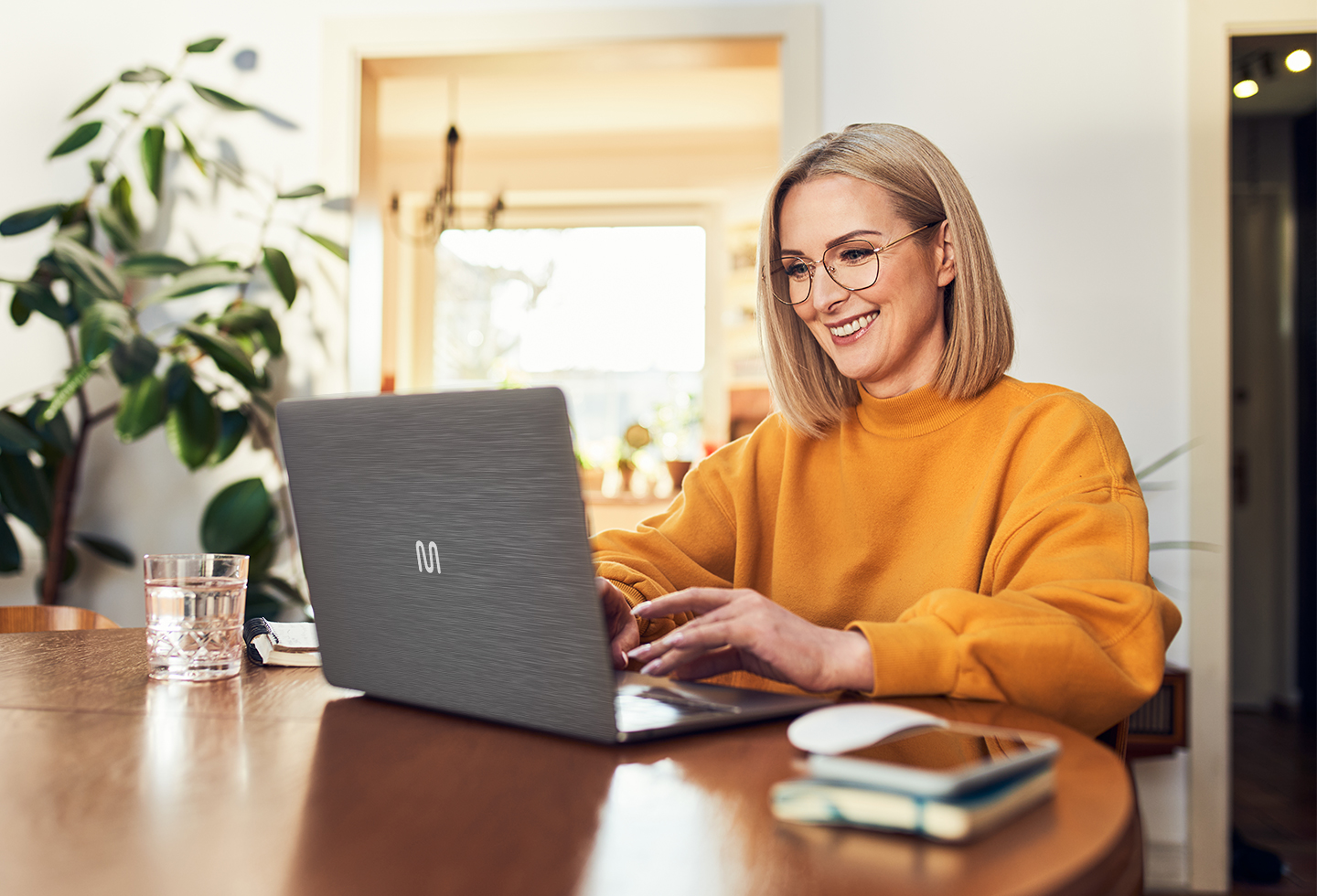 Uma mulher de óculos está sentada em uma mesa com um laptop.