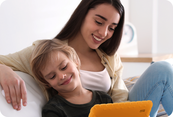 Mãe e filho sentados no sofá, em uma sala de estar, usando o Tablet Kid Pad Laranja.