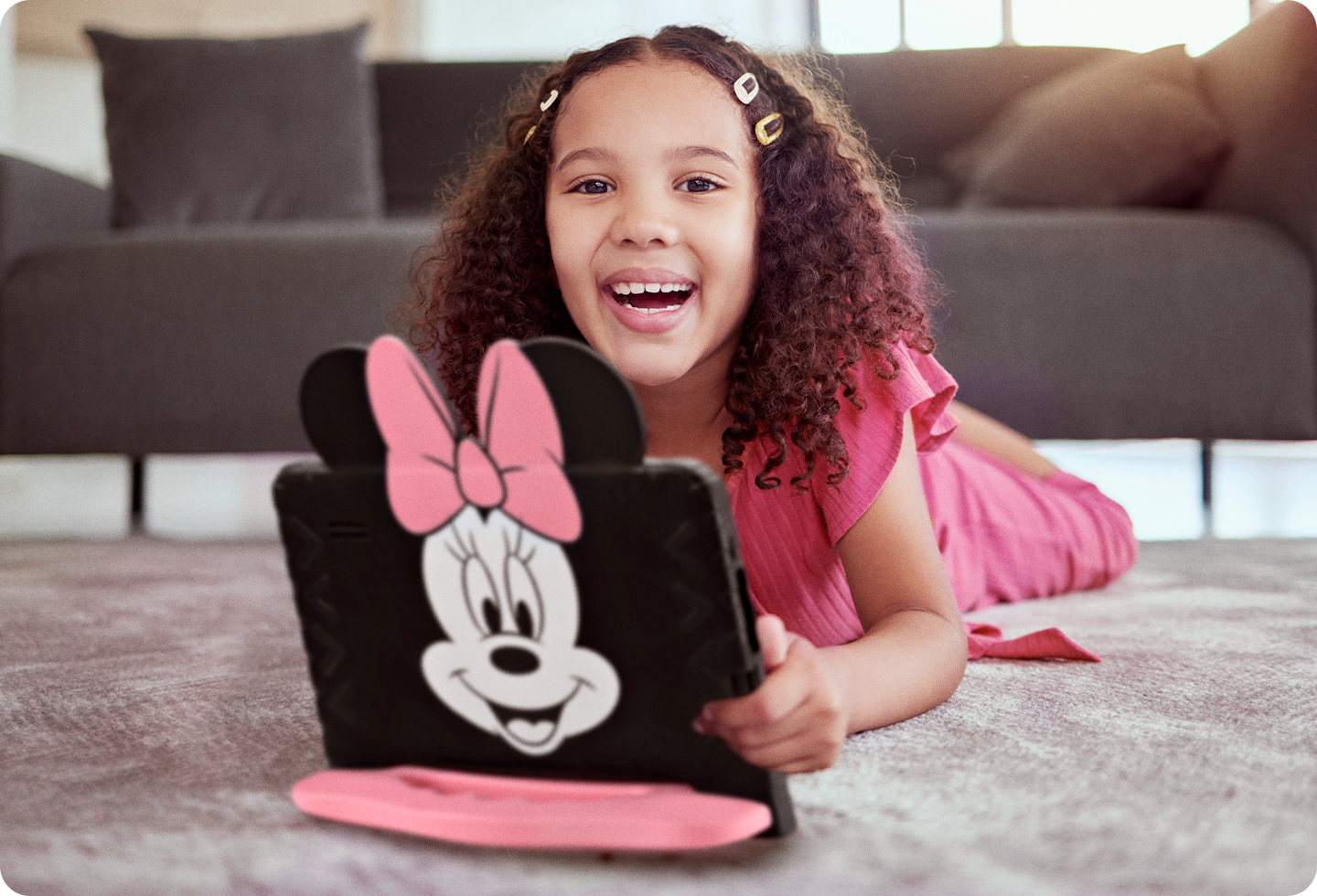 Criança deitada no tapete de uma sala de estar mexendo com o Tablet Minnie aberto à sua frente.