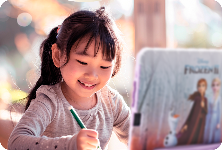 Criança sorridente e desenhando algo, enquanto há um Tablet Frozen aberto na sua frente.