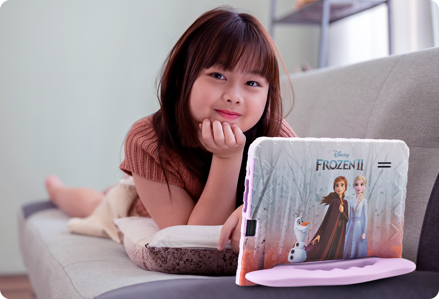 Criança deitada no sofá mexendo com o Tablet Frozen aberto à sua frente.